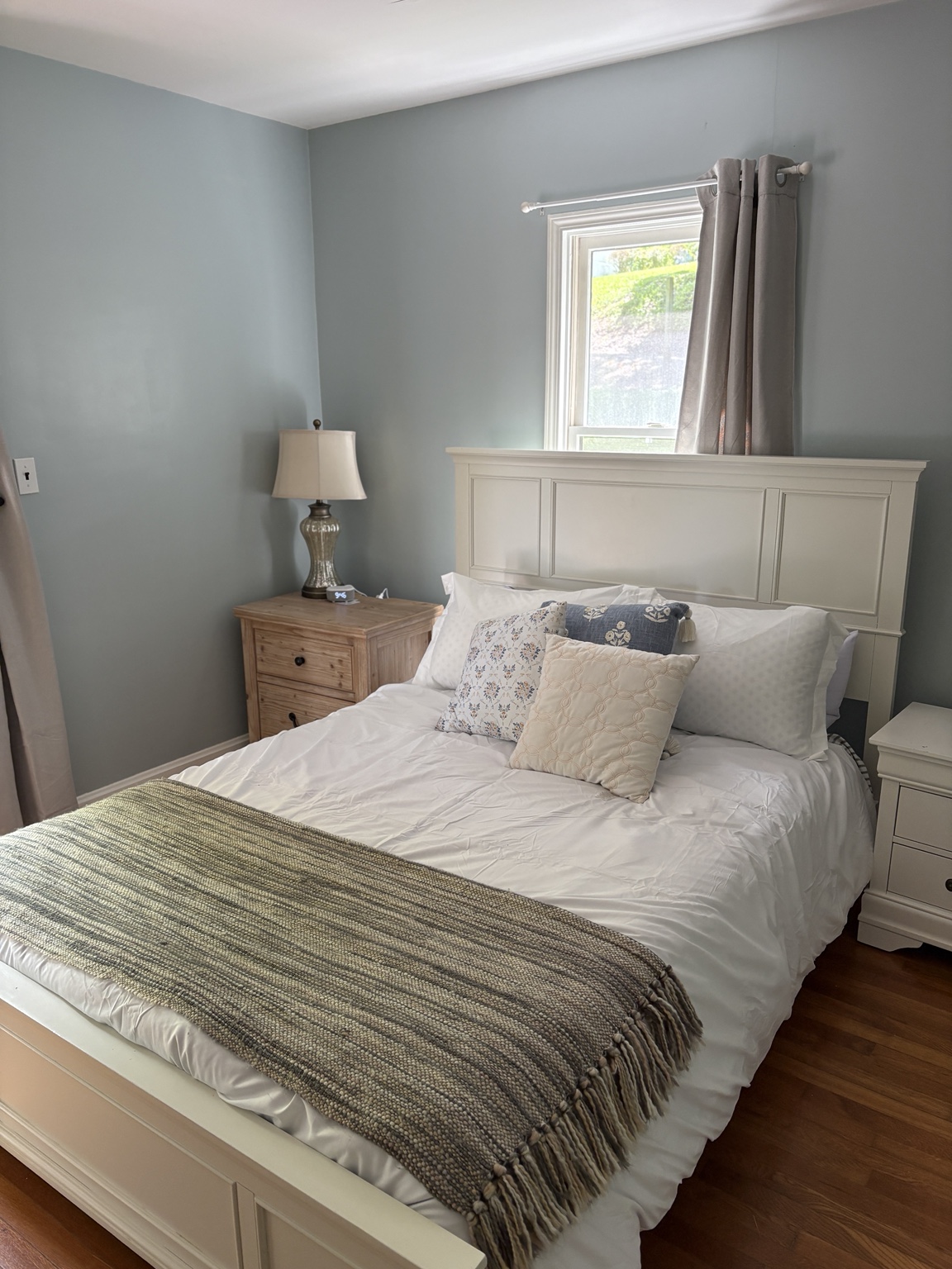 Soft blue guest bedroom with a white paneled bed and layered neutral textiles